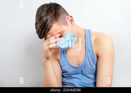 Trauriger junger Mann in einer Grippe-Maske an der Wand Im Zimmer Stockfoto