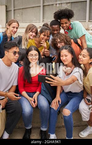 Vertikales Foto einer Gruppe von multiethnischen Studenten, die Selfies mit dem Mobiltelefon machen. Jugendliche, die ein Smartphone benutzen und Spaß zusammen haben. Stockfoto