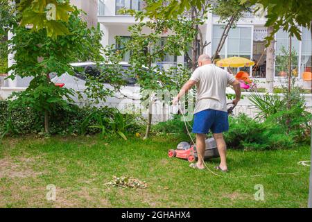 Fetter Onkel mäht den Rasen, um seinen Vater glücklich zu machen. Mann schneidet Gras mit der Maschine. Mann, der in seinem Garten arbeitet Stockfoto