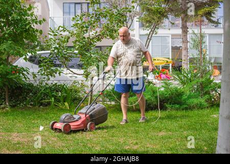 Fetter Onkel mäht den Rasen, um seinen Vater glücklich zu machen. Mann schneidet Gras mit der Maschine. Mann, der in seinem Garten arbeitet Stockfoto