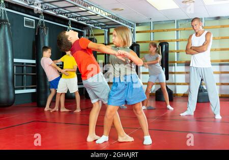 Kinder, die Selbstschutz ausüben, bewegen sich beim Training zusammen. Ihr Lehrer stand in der Nähe und beobachtete. Stockfoto