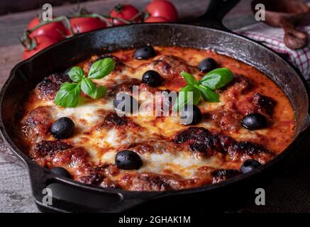 Italienische Fleischbällchen mit Tomatensauce, Mozzarella-Käse und schwarzen Oliven. Traditionelles Gericht. Serviert und gebacken in einer gusseisernen Pfanne Stockfoto