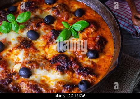 Italienische Fleischbällchen mit Tomatensauce, Mozzarella-Käse und schwarzen Oliven. Traditionelles Gericht. Serviert und gebacken in einer gusseisernen Pfanne Stockfoto