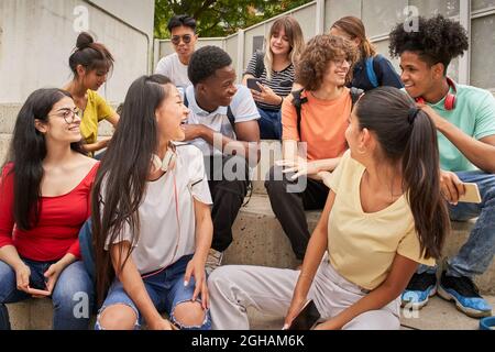 Eine multiethnische Gruppe glücklicher Studenten in einer Pause. Junge Leute lachen auf der Treppe der High School sitzen. Stockfoto