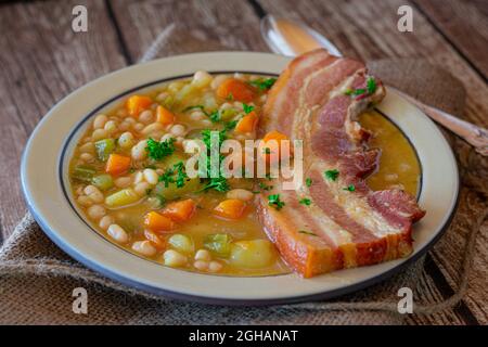 Rustikaler Eintopf mit weißen Bohnen, Wurzelgemüse und Schweinebauch auf Holztisch Stockfoto