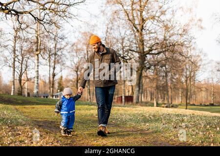 Vater und Sohn in voller Länge halten sich beim Gehen im Park die Hände Stockfoto