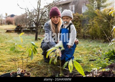 Frau mittleren Erwachsenen mit Sohn in Strickmütze und Blick auf Pflanzen im Hinterhof Stockfoto