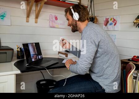 Lächelnder Mann, der zu Hause mit einer Freundin über einen Laptop telefonieren kann Stockfoto