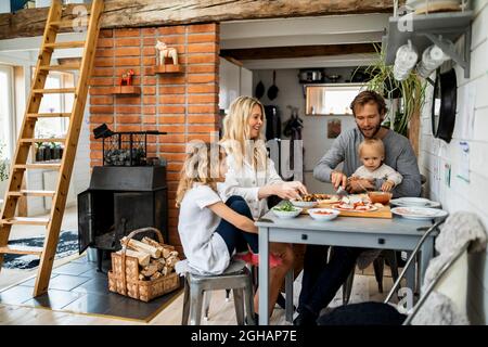 Familie bereitet Pizza zu, während sie zusammen am Tisch zu Hause sitzt Stockfoto