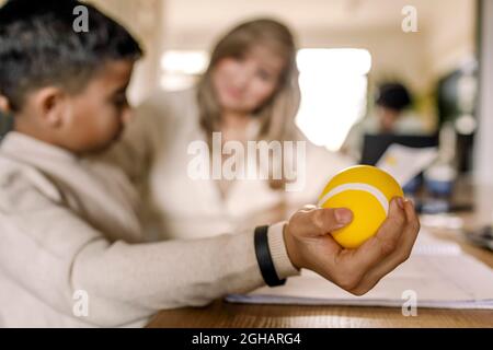 Vorpubertär Junge hält Stress Ball sitzen von der Mutter zu Hause Stockfoto