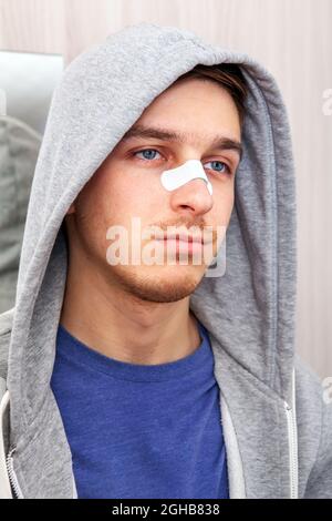 Trauriger junger Mann mit einem klebenden Gips auf der Nase in der Nähe des Spiegels im Haus Stockfoto