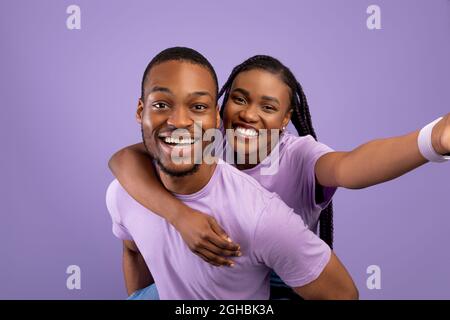 Schwarzes Paar, das Selfie macht, Frau, die auf dem Rücken des Mannes reitet Stockfoto