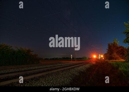 Milkyway mit seinem galaktischen Zentrum über einer einsamen Eisenbahnstrecke, die in einer sternenklaren Nacht über dem Stoppsignal steht. Stockfoto