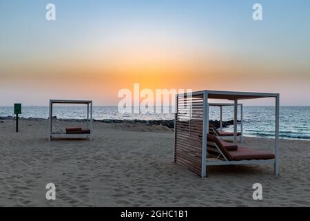 Leerer Sandstrand in Dubai mit doppelten Sonnenliegen, auf der neuen künstlichen Bluewaters Island, keine Menschen aufgrund einer Coronavirus COVID-19 Pandemie, goldener Sonnenuntergang. Stockfoto