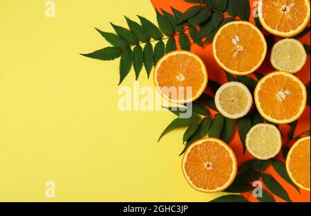 Hälften von Zitronen und Orangen mit grünen Blättern auf einem leuchtend gelb-orangen Hintergrund. Speicherplatz kopieren. Stockfoto