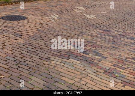 Rote und orangefarbene Ziegelsteinstraße in laufendem Anleihemuster, das die Setzung darunter zeigt, Schachtabdeckung, horizontales Aussehen Stockfoto