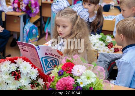 Die erste Klassenerin sitzt an ihrem Schreibtisch im Klassenzimmer und liest das Alphabet. Ein Mädchen mit weißen Schleifen sitzt am 1. September in einer Schulstunde. Moskau, R Stockfoto