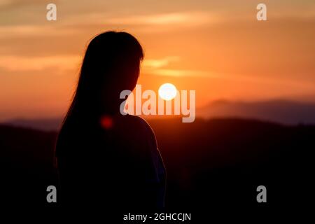 Frau steht auf dem Berg und beobachtet den nebligen Sonnenuntergang. Silhouette nachdenklich Mädchen Stockfoto