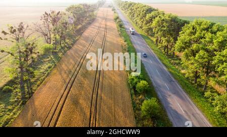 Luftdrohnenflug über Highway, Weizenfeld und grüne Bäume bei Sonnenuntergang Stockfoto