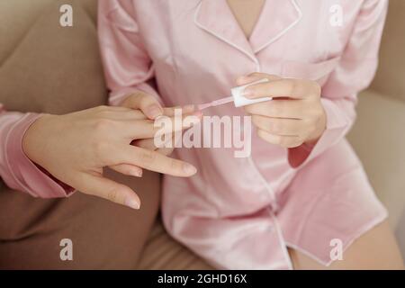 Hände der Frau, die transparente Basis auf die Nägel ihres Freundes aufbringen, wenn sie zu Hause Maniküre machen Stockfoto