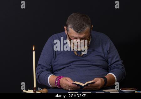 Schönes, dezernes Porträt eines älteren Mannes - Wahrsager, der ein kleines Buch liest, bevor er eine Karomantie macht Stockfoto