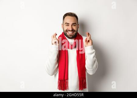 Weihnachtsferien und Neujahrskonzept. Hoffnungsvoller Mann, der Wunsch mit gekreuzten Fingern macht, auf Geschenke wartet, über weißem Hintergrund steht Stockfoto