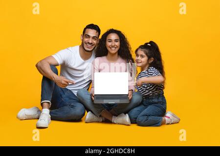 Fröhliche arabische Familie mit kleiner Tochter, die einen Laptop mit leerem weißen Bildschirm zeigt Stockfoto