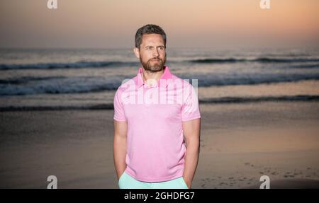 Charismatischer Mann mit Bart bei Sonnenuntergang über Meer. Unrasiert Kerl am Morgen Strand. Stockfoto