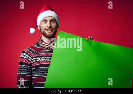 Fröhlicher Mann in einem weihnachtshut mit grünem Mockup rotem Hintergrund Stockfoto