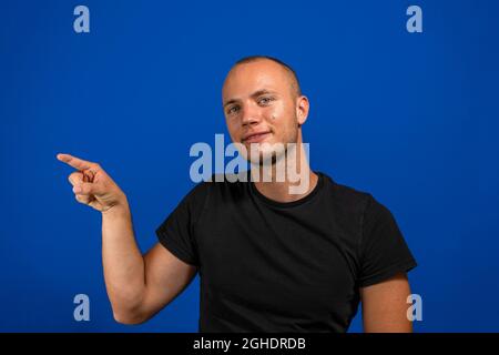 Junger, hübscher Mann, der ein legeres Hemd auf einem isolierten blauen Hintergrund trägt, ist fröhlich mit einem Lächeln auf dem Gesicht, das mit Hand und Finger zur Seite zeigt Stockfoto