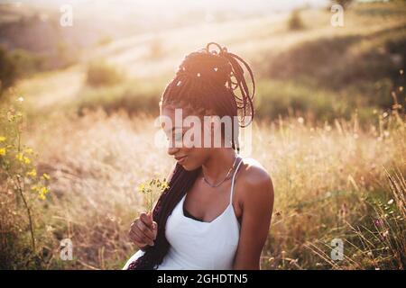 Schöne schwarze junge Frau im Park Porträt lange Zöpfe lächelnde Blume Stockfoto