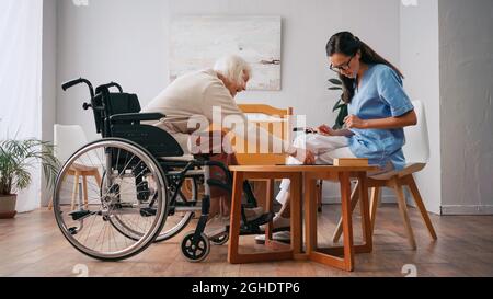 Junge Krankenschwester und glückliche ältere Frau spielen Brettspiel Stockfoto