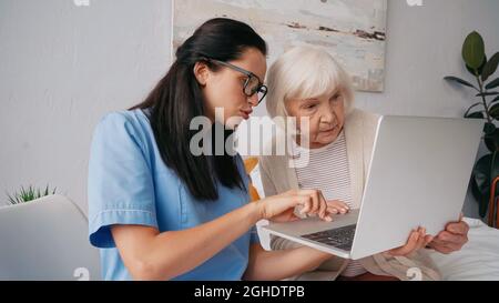 Brunette Krankenschwester zeigt im Alter Frau, wie man Laptop verwenden Stockfoto