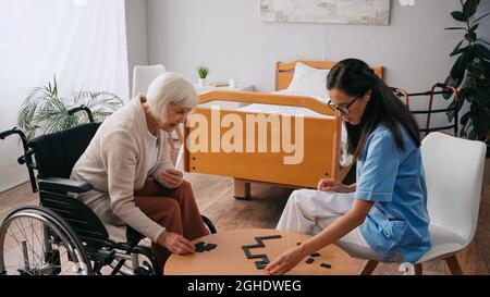 Ältere Frau im Rollstuhl, die mit einer jungen Krankenschwester Dominosteine spielt Stockfoto
