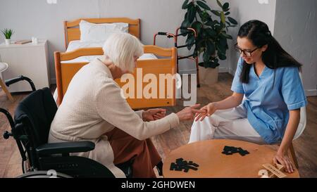 Ältere Frau im Rollstuhl, die mit einer brünette Krankenschwester Dominosteine spielt Stockfoto