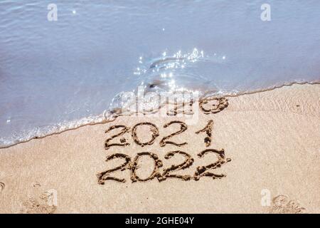 Die Zahlen 2021, 2022 werden auf den Sand gezogen und von der Welle, dem Symbol des neuen Jahres, dem Jahreswechsel, weggespült Stockfoto