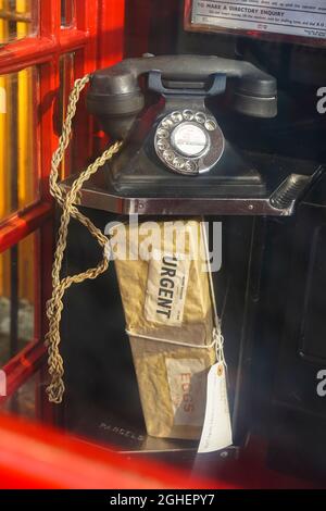 Blick durch das Glas einer alten, traditionellen britischen roten Telefonzelle und Blick auf ein dringendes Paket, das im Regal unter dem alten Hörer zurückgelassen wurde. Stockfoto