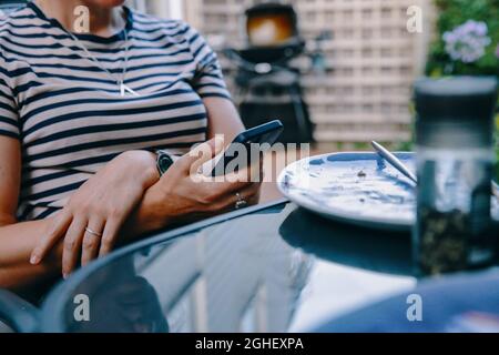 Eine Frau überprüft ihr iphone-Smartphone am Esstisch draußen in London, England Stockfoto