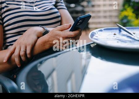 Eine Frau überprüft ihr iphone-Smartphone am Esstisch draußen in London, England Stockfoto