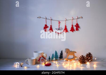 Weihnachtskomposition auf dem Tisch. Graues Schaukelpferd aus Holz, vier kleine künstliche schneebedeckte Bäume, Engel, Girlande und Becher Stockfoto