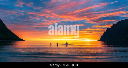 Freunde, die Spaß haben, im Meer gegen den bunten Himmel bei Sonnenuntergang zu planschen, Ersfjord, Senja, Troms County, Norwegen Stockfoto