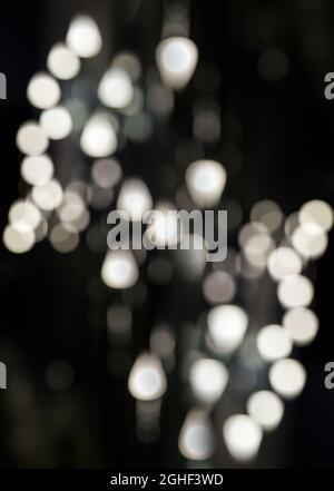 Rundes und dreieckiges Bokeh auf schwarzem Hintergrund. Abstrakter Hintergrund mit Bokeh-defokussierten Lichtern. Vertikales Foto Stockfoto