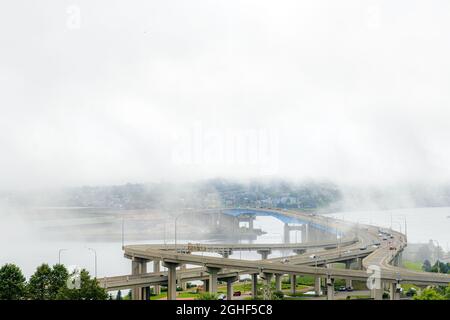 Saint John, NB, Kanada - 14. August 2021: Nebel schwebt über der Saint John Harbour Bridge. Autos fahren auf der Brücke. Gegenüberliegender Strand durch Nebel sichtbar. Stockfoto