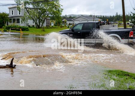 Saint John, NB, Kanada - 2. September 2021: Ein LKW fährt durch eine überflutete Straße. LKW-Reifen sprühen Wasser. Wasser sprudelt aus verborgenem Sturmabfluss. Stockfoto