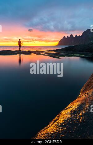 Mann, der auf Felsen am Meer steht und die Zähne des Teufels bei der Mitternachtssonne fotografiert, Tungeneset, Senja, Kreis Troms, Norwegen Stockfoto