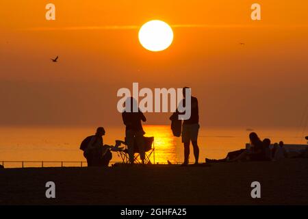 West Bay, Dorset, Großbritannien. September 2021. Wetter in Großbritannien. Die Strandbesucher werden im Badeort West Bay in Dorset nach einem Tag glühender, heißer Sonne während einer Mini-Hitzewelle vor einem goldorangen Sonnenuntergang geschildet. Bildnachweis: Graham Hunt/Alamy Live News Stockfoto