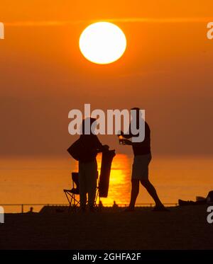 West Bay, Dorset, Großbritannien. September 2021. Wetter in Großbritannien. Die Strandbesucher werden im Badeort West Bay in Dorset nach einem Tag glühender, heißer Sonne während einer Mini-Hitzewelle vor einem goldorangen Sonnenuntergang geschildet. Bildnachweis: Graham Hunt/Alamy Live News Stockfoto