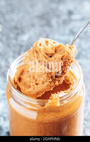 Löffel taucht in ein Glas mit knackiger Erdnussbutter. Stockfoto