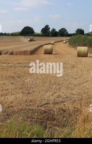 Feld, das am Sommertag in West Yorkshire, Großbritannien, von einem Mähdrescher mit unscharfer Luft und Wolken geerntet wird Stockfoto