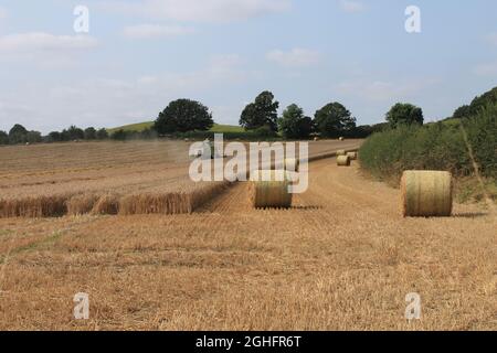 Feld, das am Sommertag in West Yorkshire, Großbritannien, von einem Mähdrescher mit unscharfer Luft und Wolken geerntet wird Stockfoto